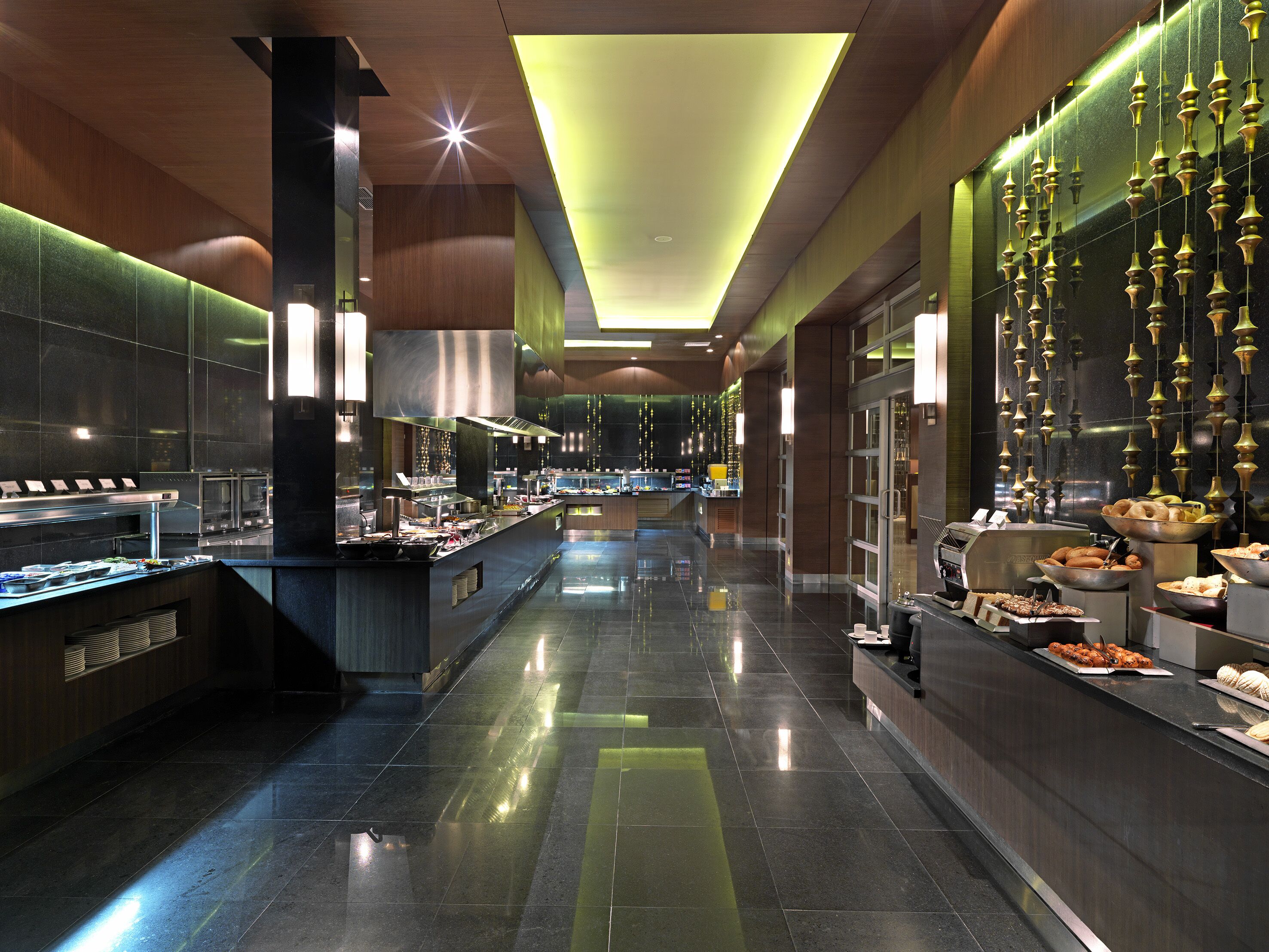Un hall d’hôtel moderne avec un long comptoir d’accueil, un espace buffet et un mur décoré de guirlandes lumineuses suspendues.