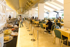 Een ruime eetruimte met meerdere tafels en stoelen, een buffet en een ober die gasten bedient.