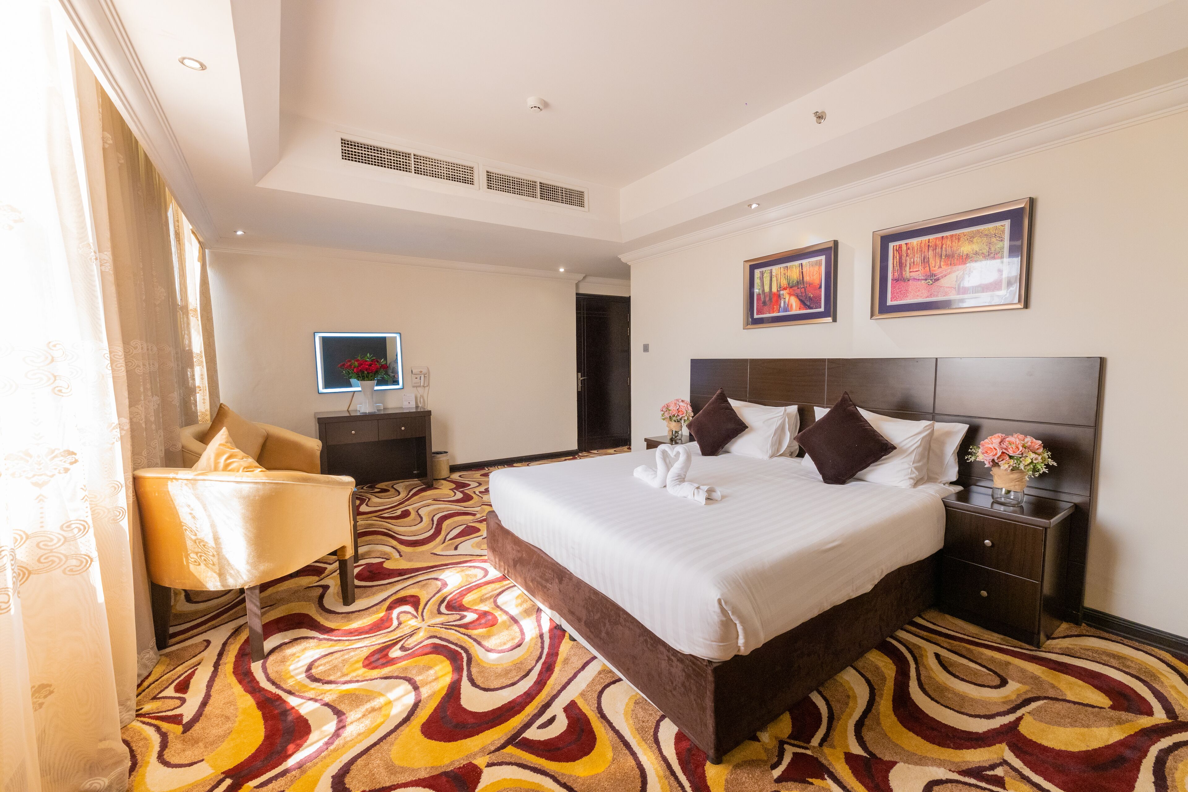 Una habitación de hotel con una cama grande, una mesita de noche con un florero, una silla y un televisor.