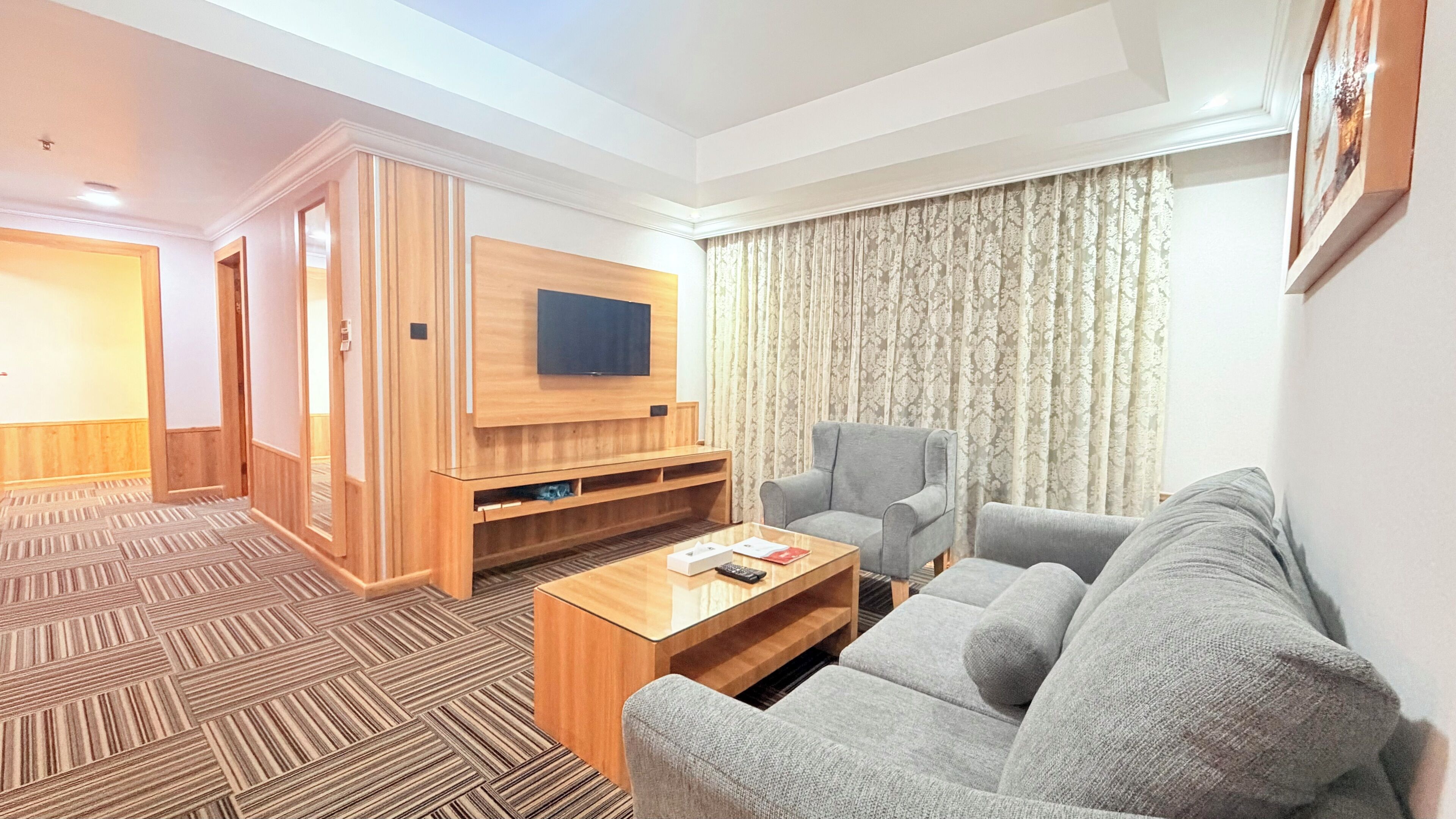 Habitació d'hotel amb un moble d'entreteniment de fusta, un sofà gris, una taula de cafè i una televisió.