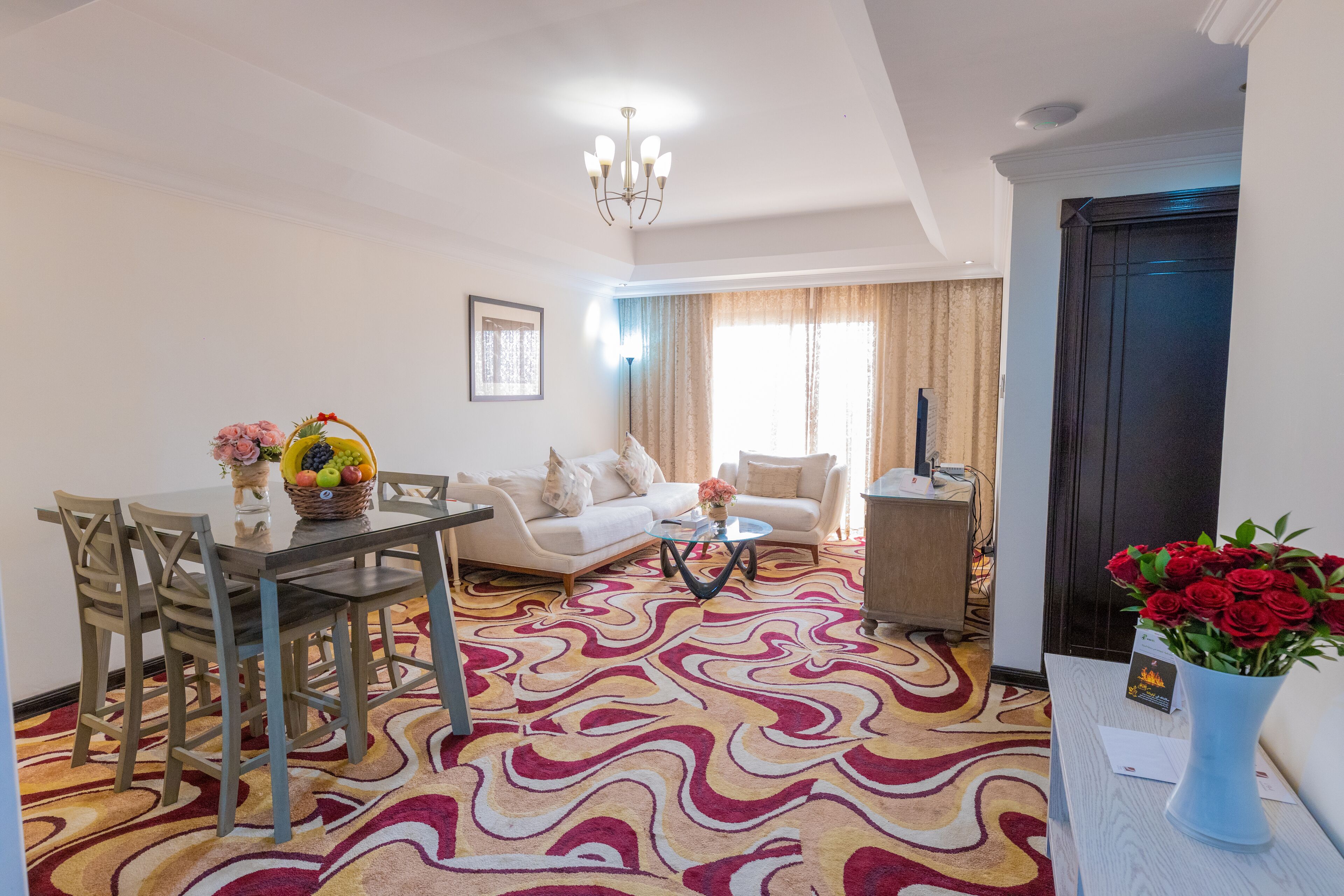 A living room with a glass dining table, beige sofas, and a patterned carpet.