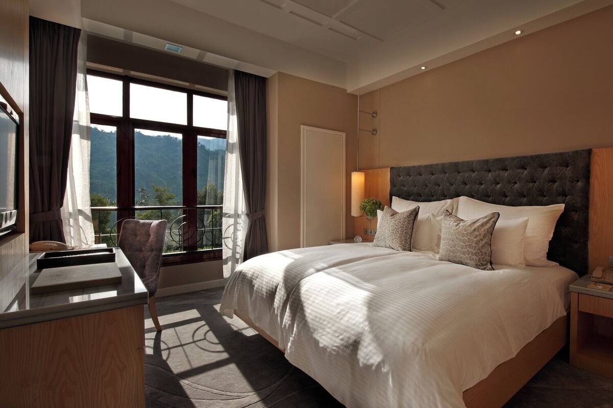 Une chambre d’hôtel moderne, dotée d’un grand lit, d’un bureau et offrant une vue sur les montagnes par la fenêtre.