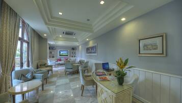 A spacious living area with a large window, comfortable seating, a glass coffee table, and a laptop on a desk.