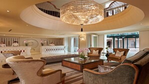 A spacious lobby with a central coffee table, comfortable seating, a reception desk, and a large chandelier.