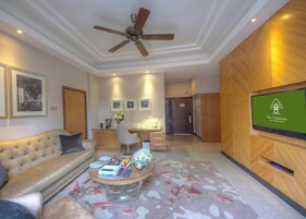 Vestíbulo de hotel con un sofá, una mesa de centro con libros y flores, un escritorio con una computadora, cuadros en la pared y un televisor mostrando 'The Chateau Spa & Wellness Resort'.