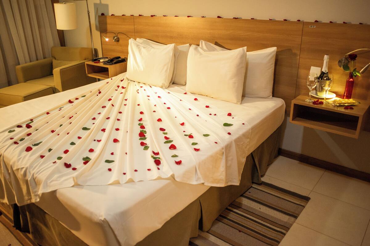 A hotel room with a neatly made bed, a bedside table with a bottle and glass, and a chair.
