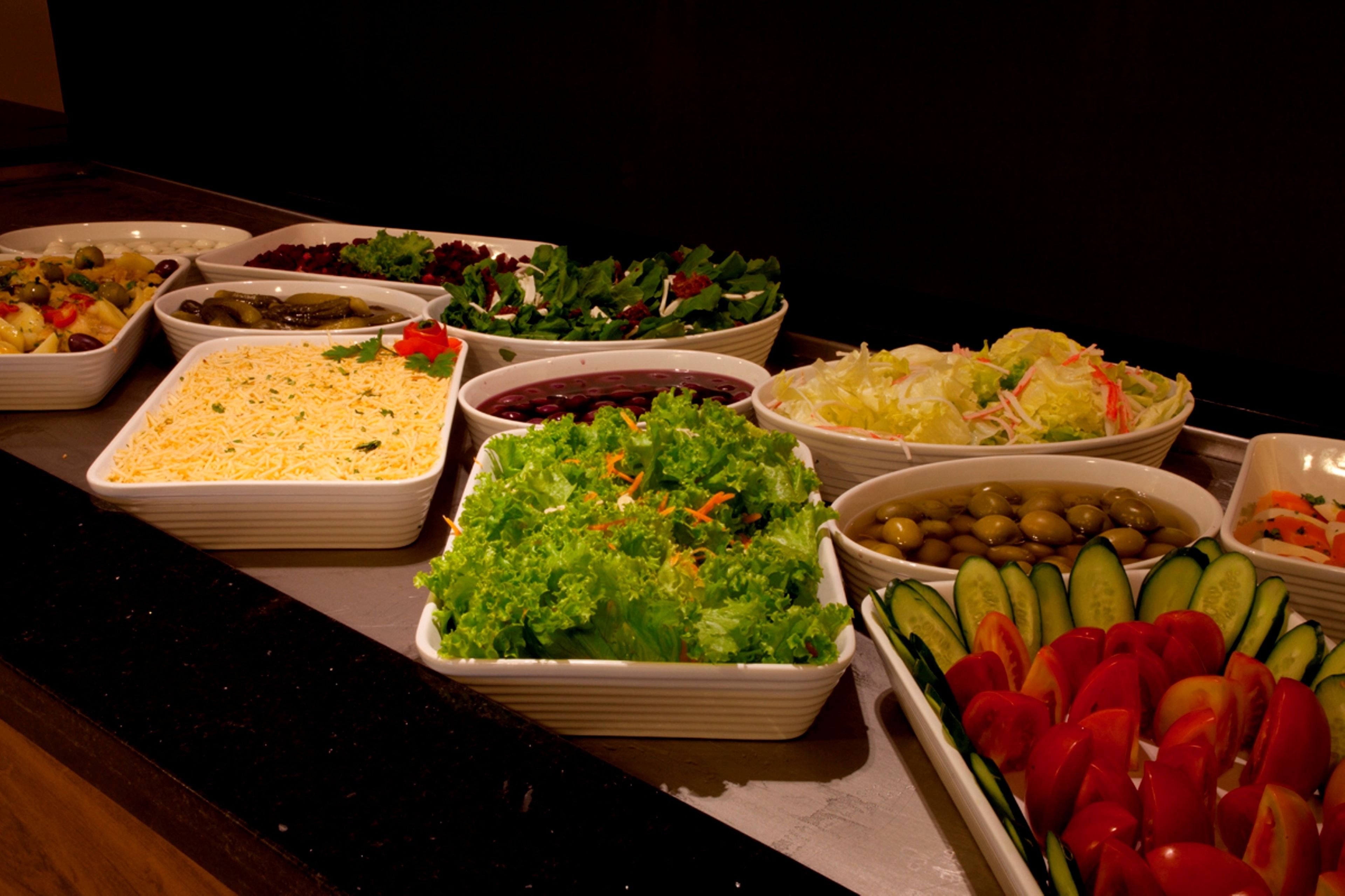 Een buffet met verschillende gerechten, waaronder salades, groenten en een ovenschotel.