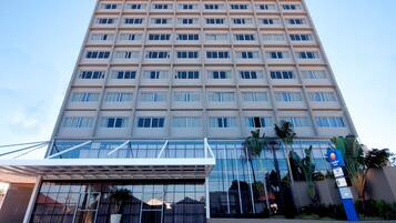Un edificio moderno de gran altura con fachada de vidrio, varios pisos y una entrada destacada con vestíbulo cubierto.