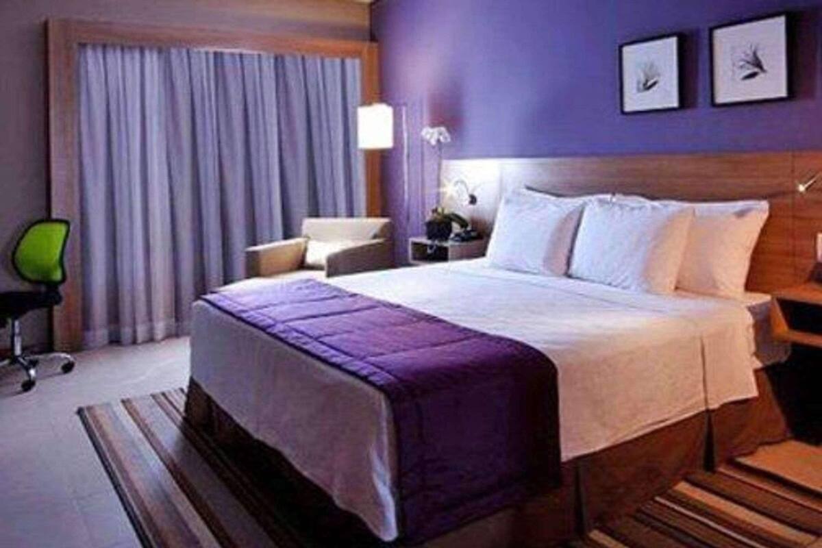 A hotel room with a bed, a chair, a nightstand, and a window with curtains.