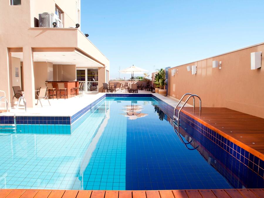 A swimming pool with blue tiles, wooden deck, and outdoor seating area with chairs and umbrellas.