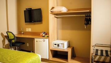 A compact hotel room with a bed, a desk with a computer, a small fridge, a microwave, and a TV mounted on the wall.