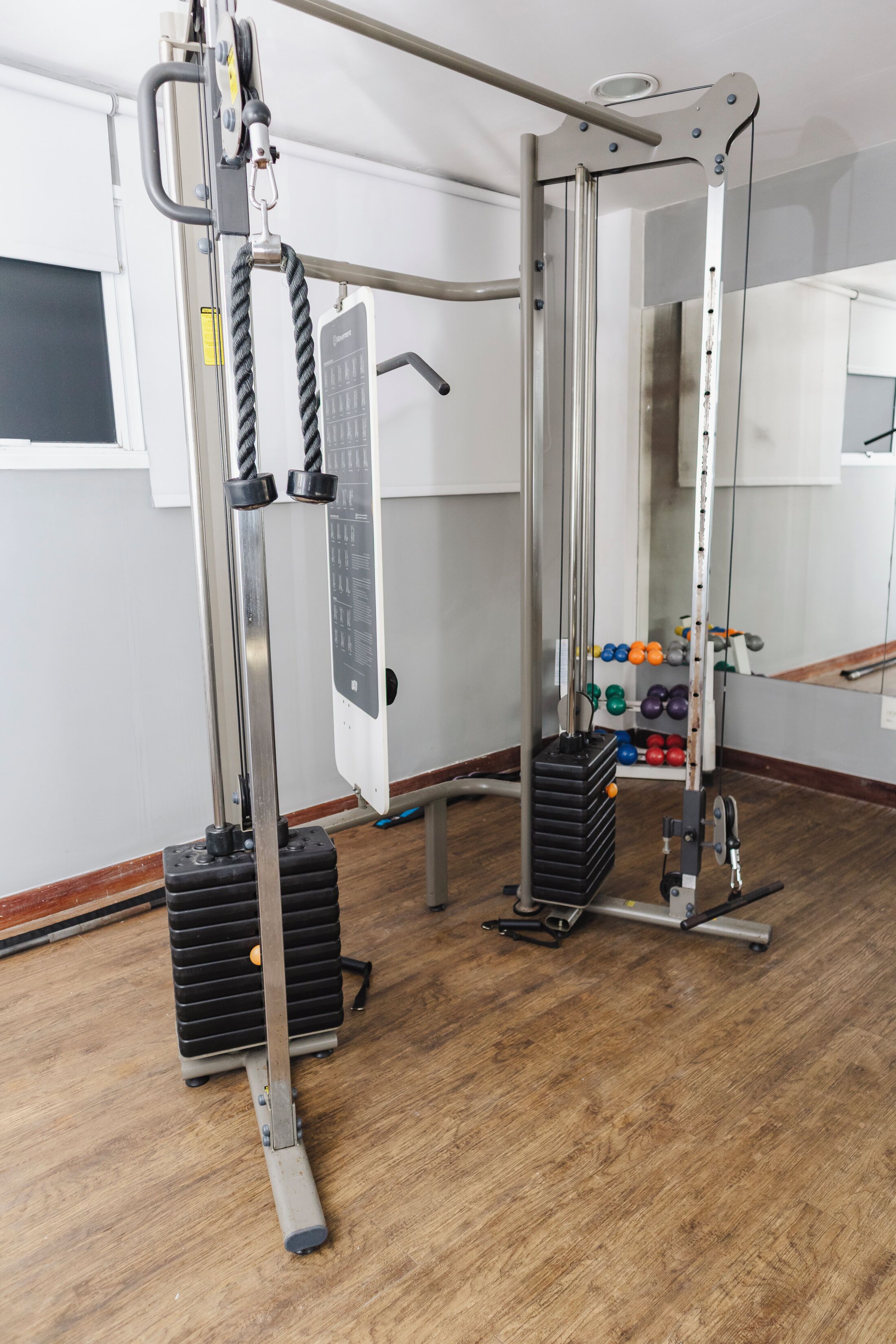 Un gimnasio con equipo de levantamiento de pesas, incluyendo una jaula para sentadillas y una máquina de poleas.
