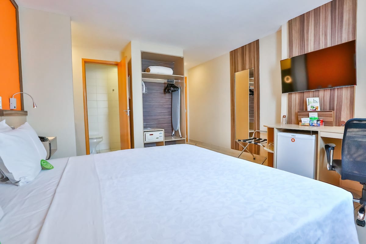 A hotel room with a bed, a desk, a mini-fridge, a TV, and a wardrobe.