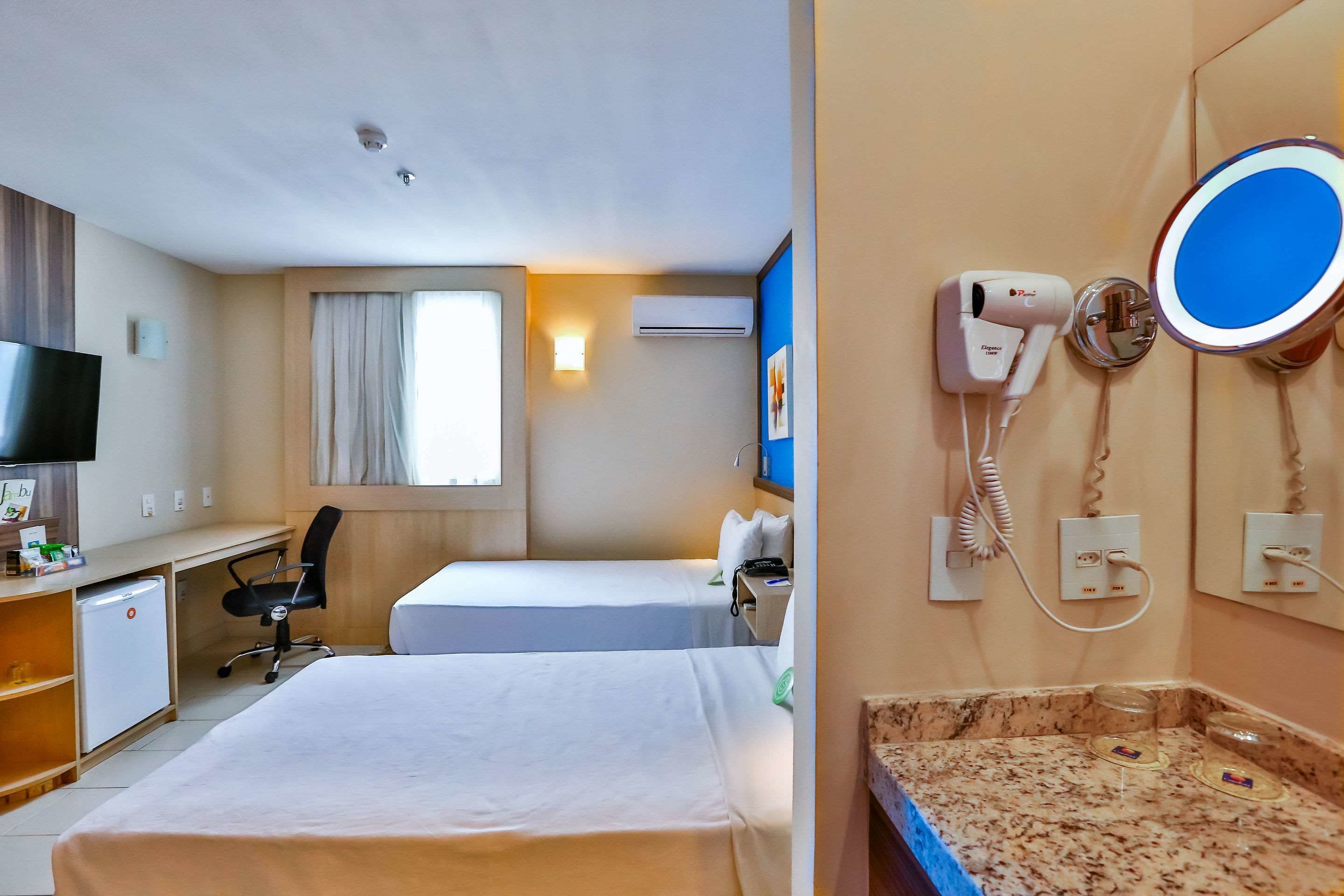 Une chambre d’hôtel avec deux lits, un bureau, une télévision, un sèche-cheveux et un miroir.