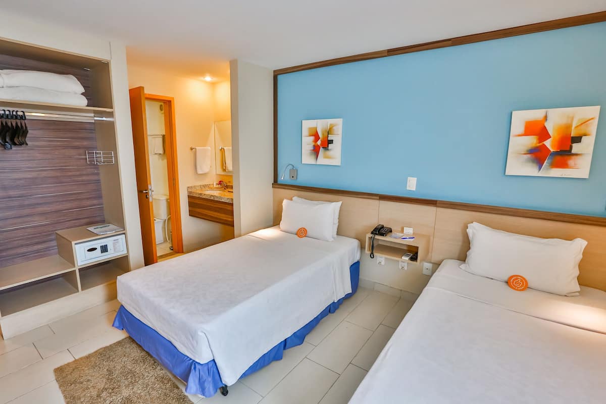 A hotel room with two beds, a wardrobe, a bathroom, and abstract wall art.