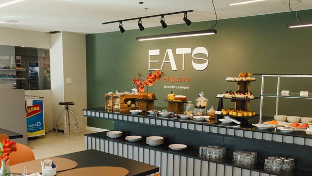 A modern breakfast area with a buffet setup, including various food items and a seating area with orange chairs. - Comfort Hotel Campos Dos Goytacazes (Campos)