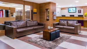 A modern hotel lobby with leather sofas, a reception desk, and a television screen. - Comfort Hotel Campos Dos Goytacazes (Campos)