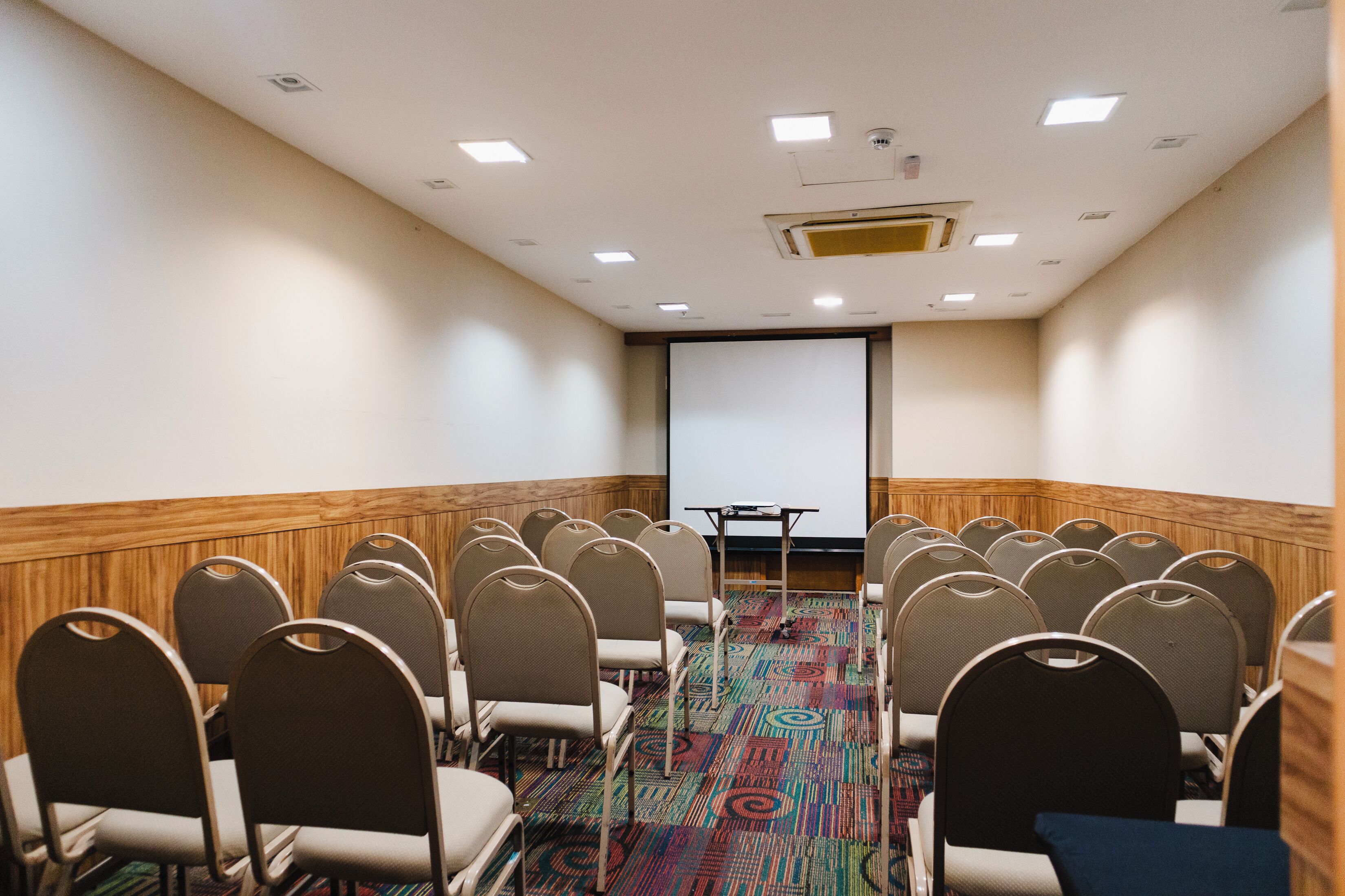 A conference room with rows of chairs, a projector screen, and a carpeted floor.
