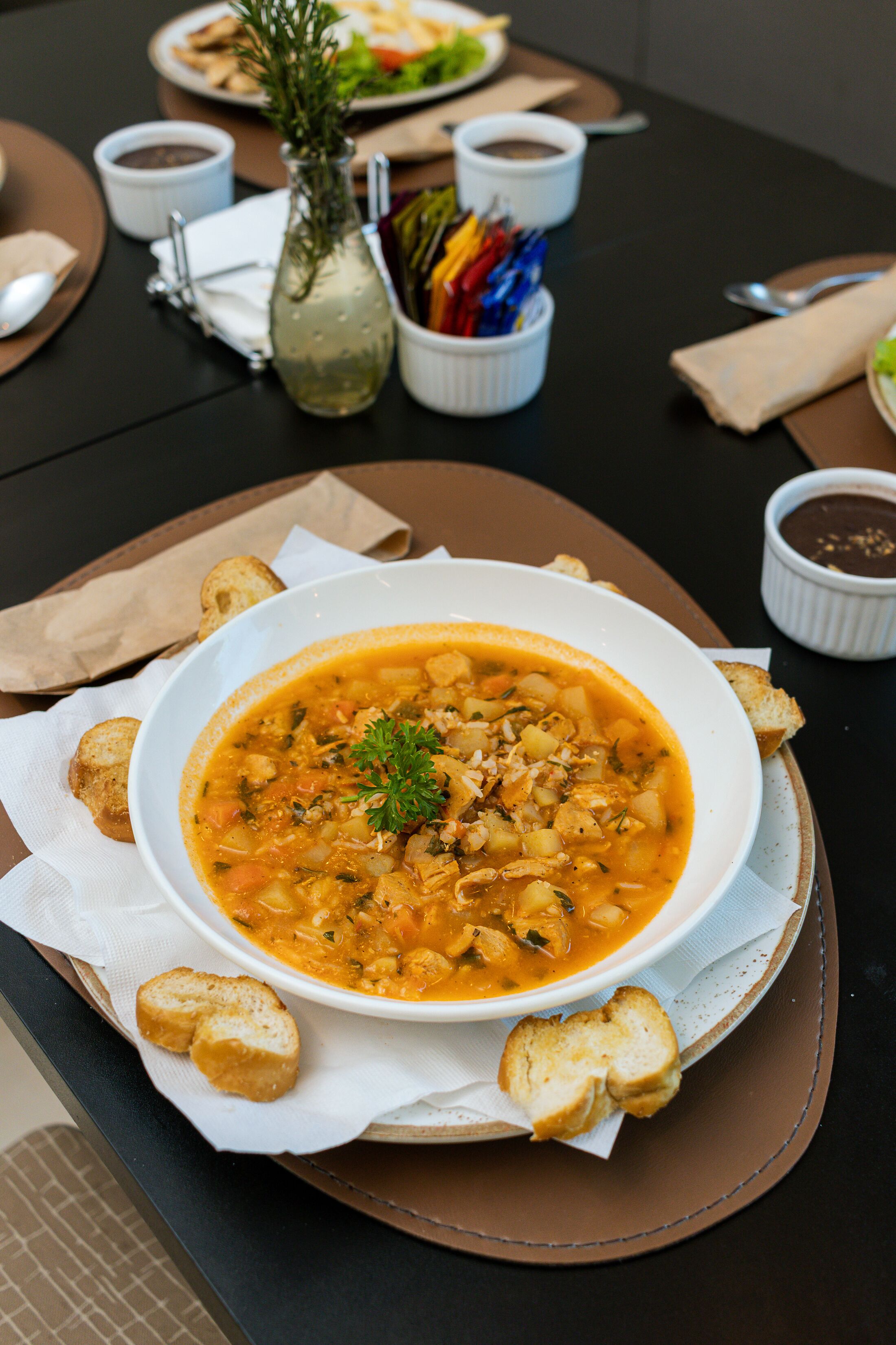 A table with a bowl of soup, bread, and condiments.