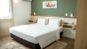 A hotel room with a large bed, bedside tables, a wall-mounted air conditioner, a painting, and a small shelf with a phone and a lamp. - Comfort Hotel Campos Dos Goytacazes (Campos)