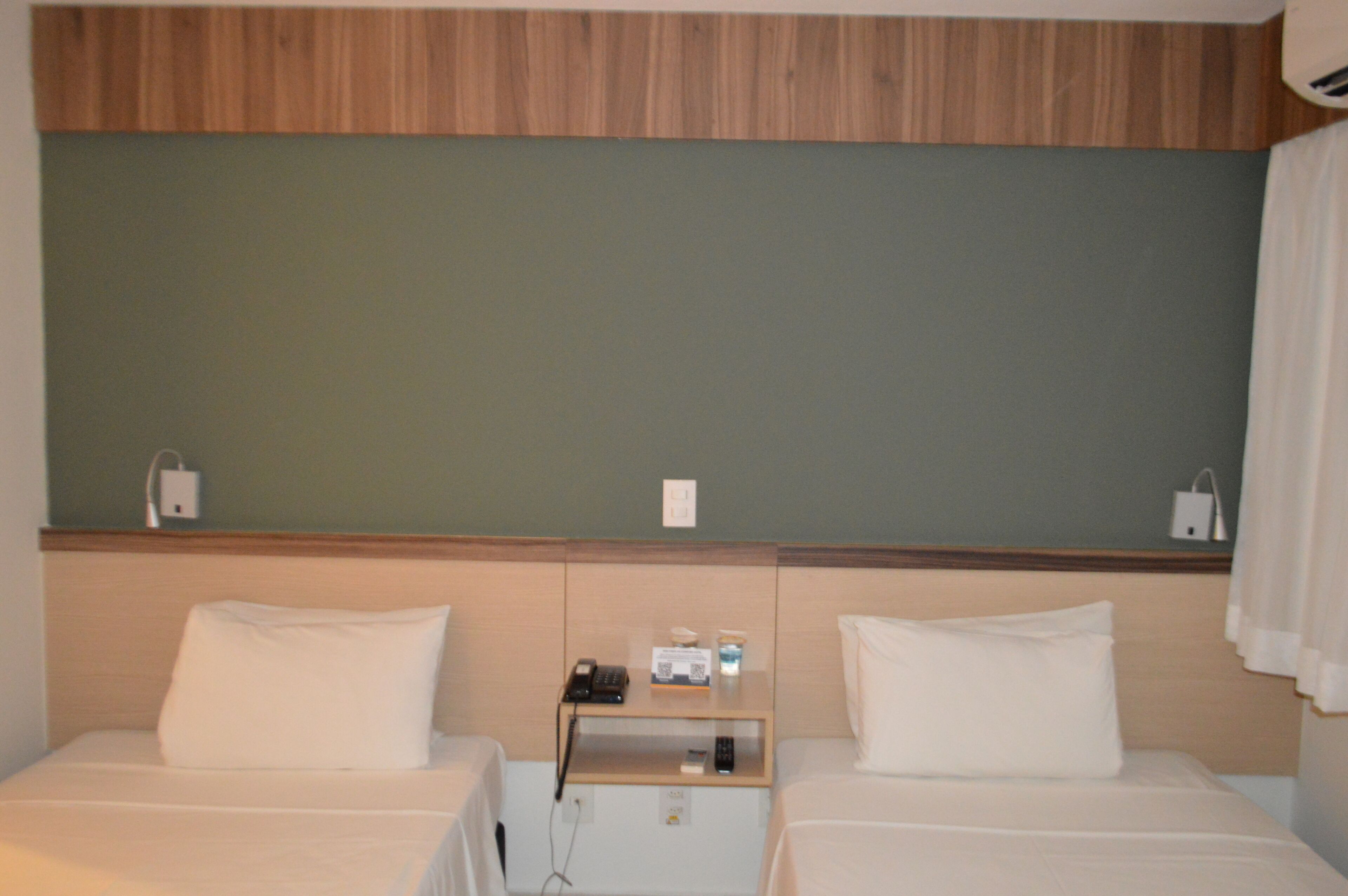 Ein Hotelzimmer mit zwei Betten, einem Holz-Kopfteil, einem kleinen Nachttisch mit Telefon, Fernbedienung und Taschentuchbox.