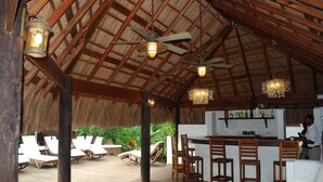 Eine Holzterrasse mit Liegestühlen, einer Bar und Deckenventilatoren.