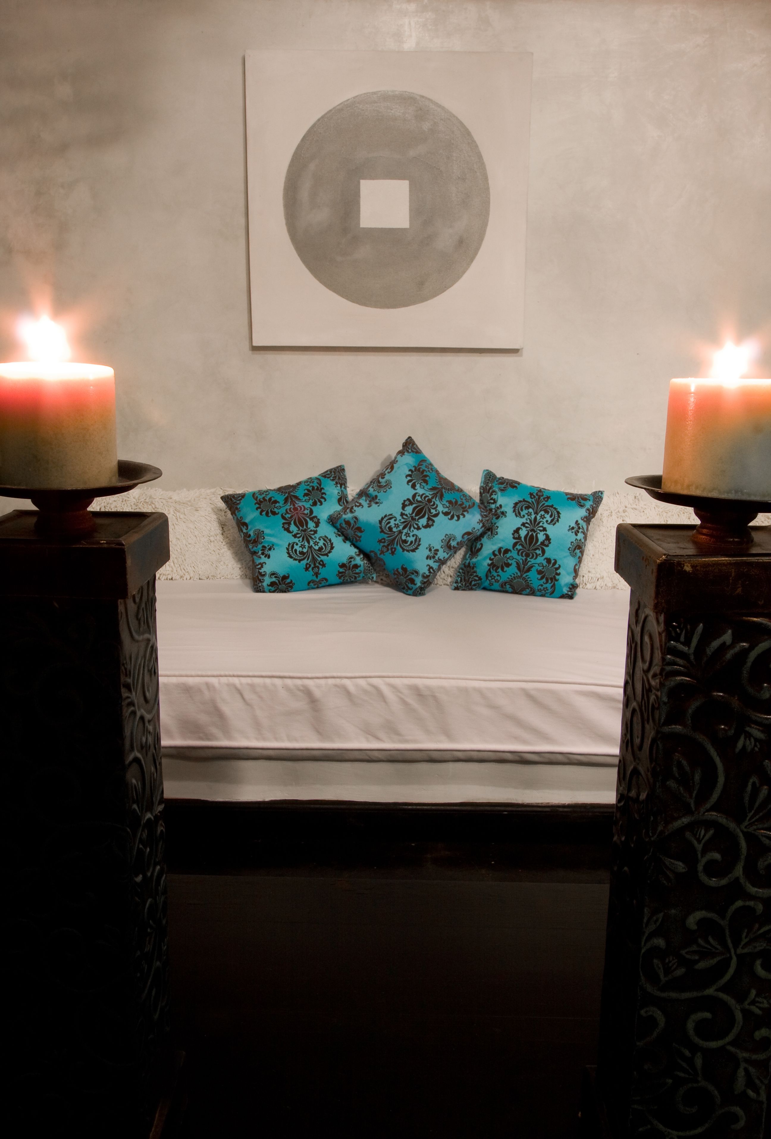 Un lit avec une literie blanche et deux coussins à motifs turquoise, encadré de deux chandeliers décoratifs où brillent des bougies allumées.