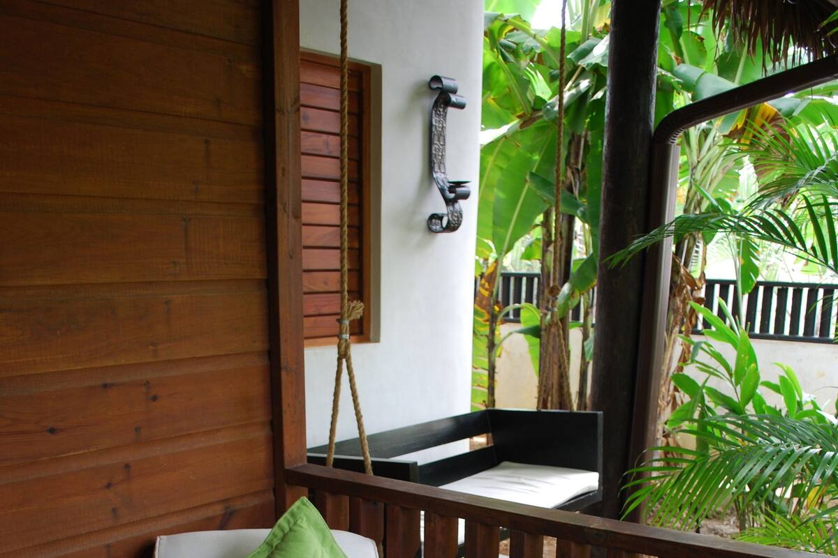 A wooden bench with a green cushion, a rope, and a wooden railing.