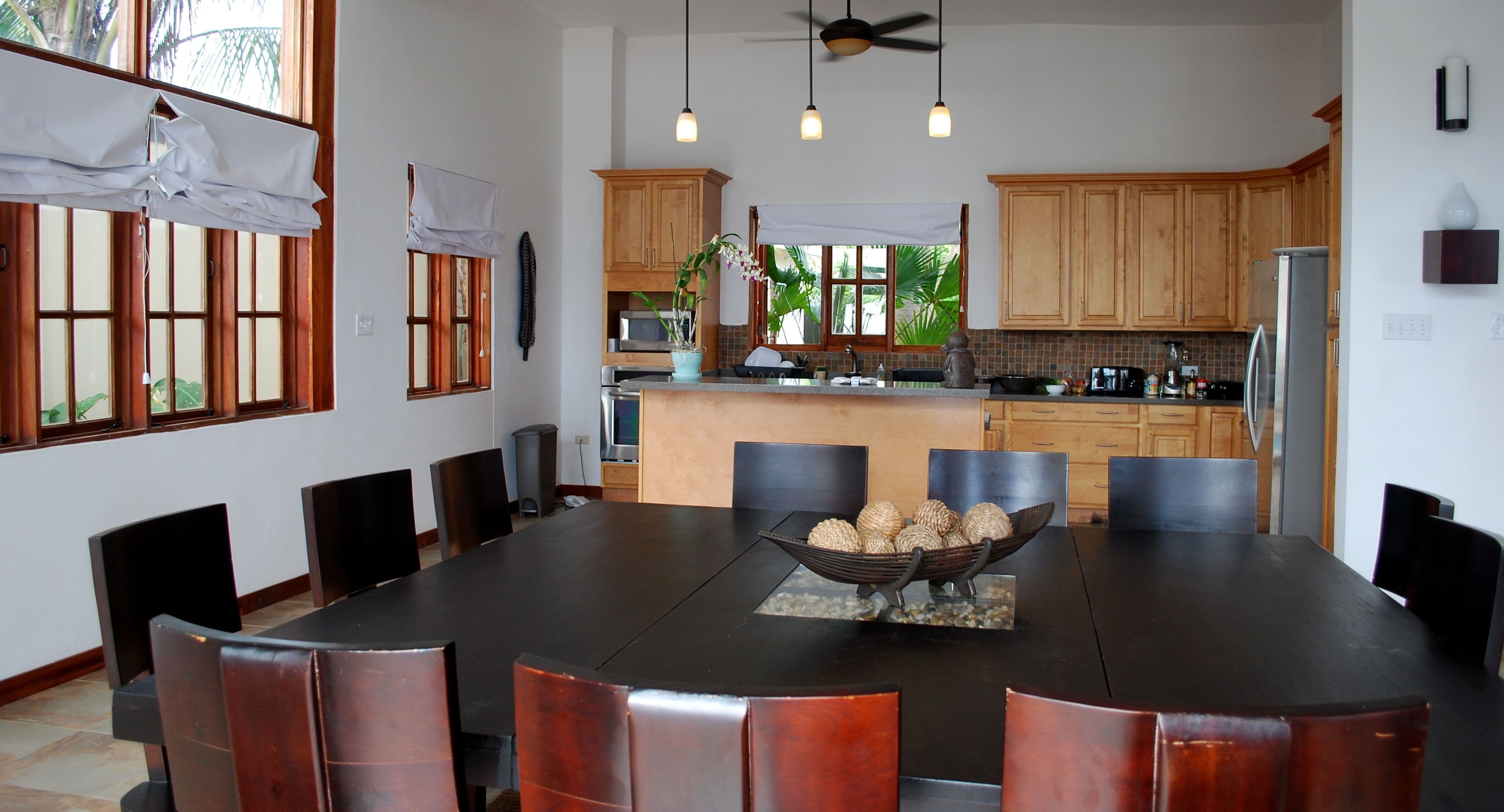 A modern kitchen with wooden cabinets, a central island, and a dining area with a large table and chairs.