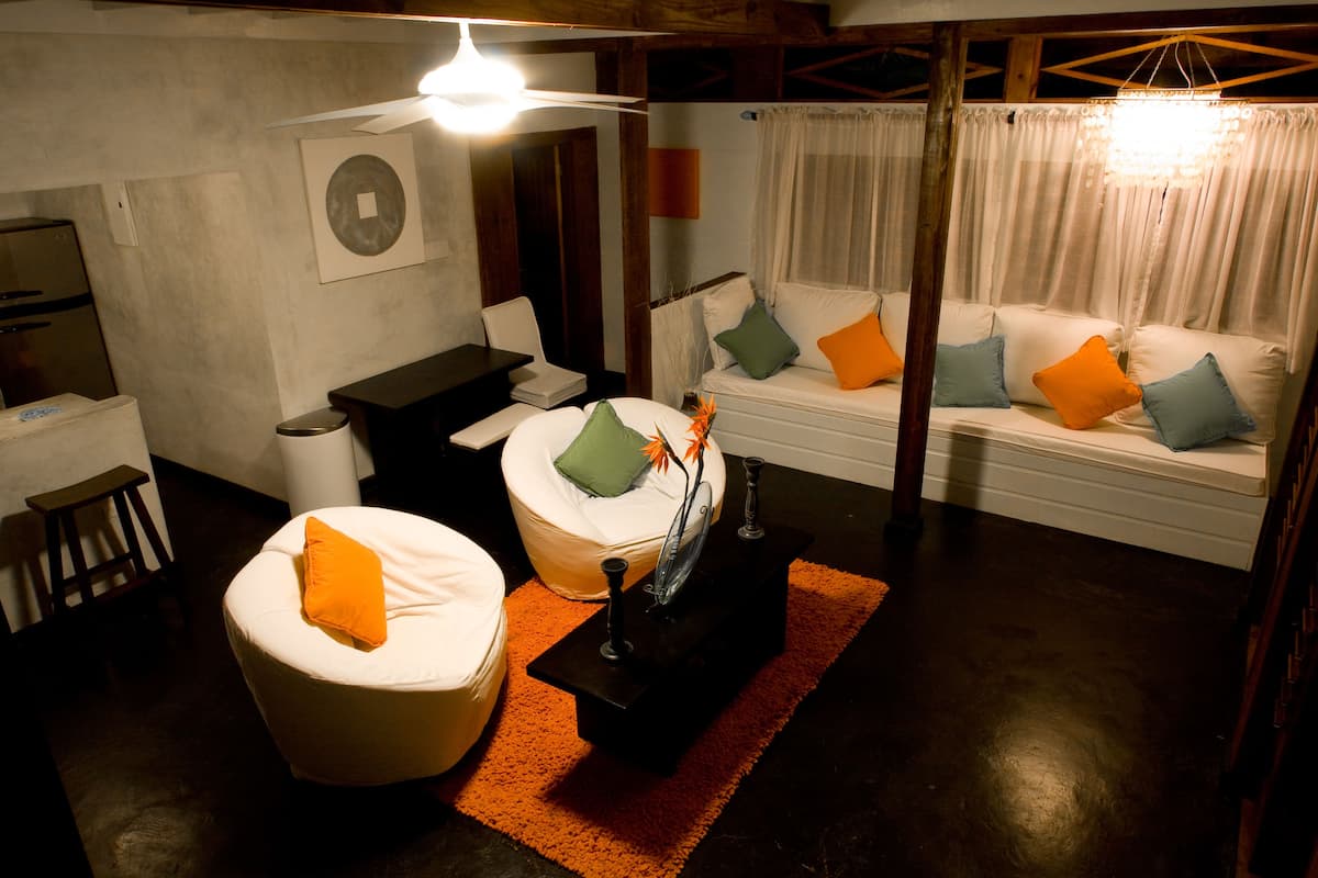 A modern living room with a white sofa set, orange and green cushions, a small table with a decorative item, and a ceiling fan.