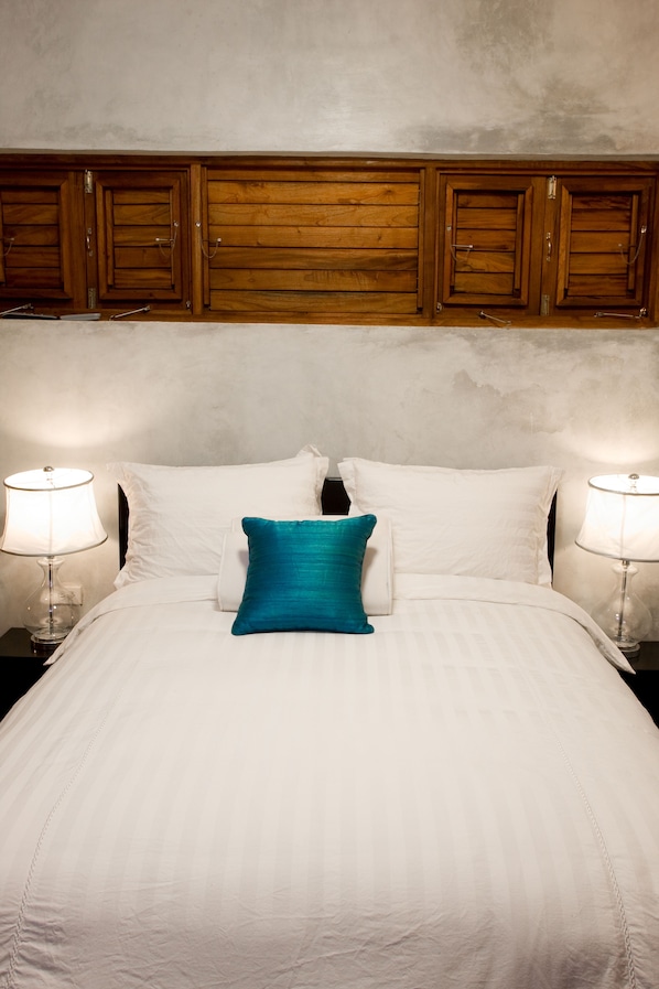 A neatly made bed with white linens and a teal accent pillow, flanked by two bedside lamps on wooden nightstands. - Villas Sur Mer (Negril)