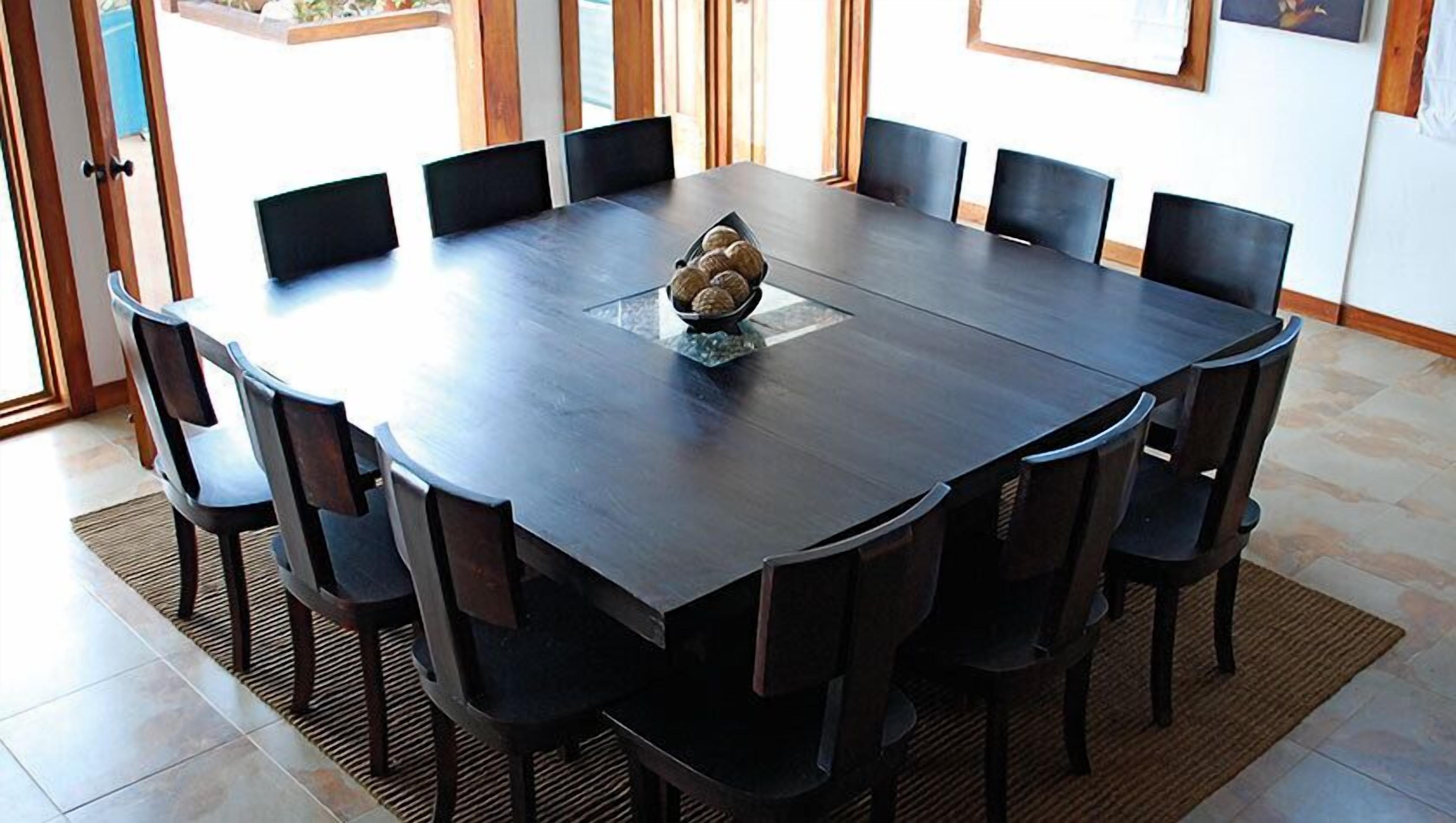 A rectangular dining table with eight chairs, a decorative bowl in the center, and a view of the outdoors through large windows.