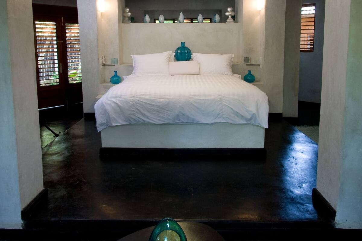 A modern bedroom with a large bed, a ceiling light fixture, and a small table with a vase.
