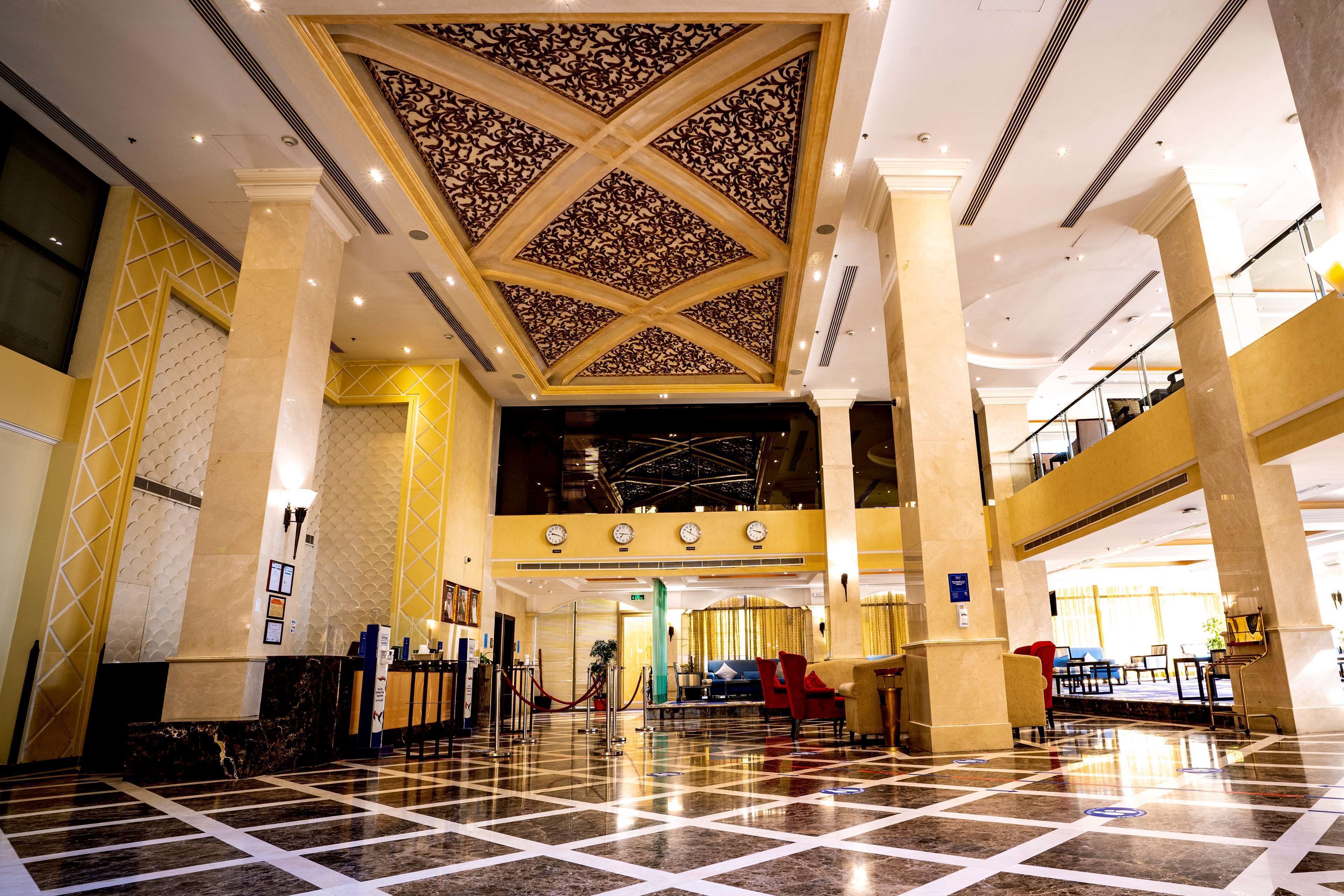 A spacious lobby with a high ceiling, marble flooring, and a reception area with a desk and chairs.