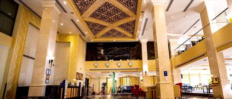 A spacious lobby with a high ceiling, marble flooring, and a reception area with a desk and chairs.