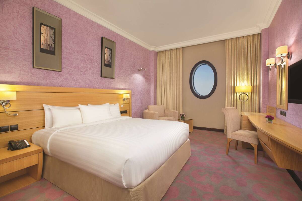 Habitación de hotel con una cama grande, un escritorio, una silla, una mesita de noche y un televisor.