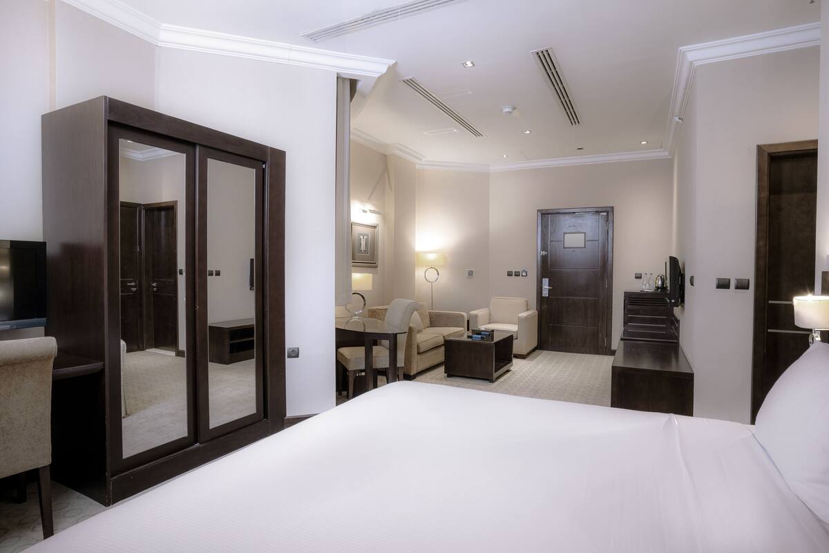 Habitación de hotel con una cama grande, un armario, un escritorio, una silla, un sofá y una escalera que conduce a otra habitación.