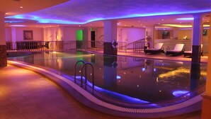 An indoor swimming pool with a curved design, surrounded by lounge chairs and a staircase leading to an upper level. - DoubleTree by Hilton Hotel Dhahran (Al Khobar)