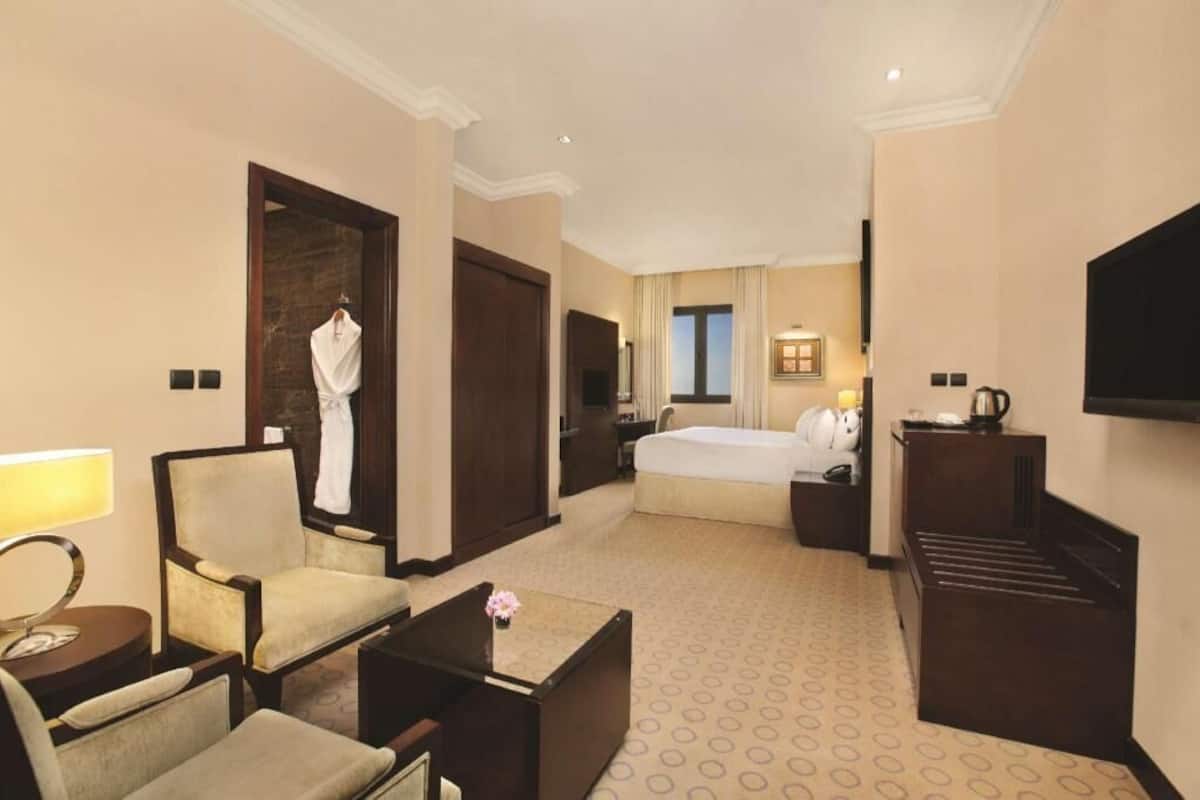 Habitación de hotel con cama, una silla, un escritorio, televisor y bata colgada en la puerta.