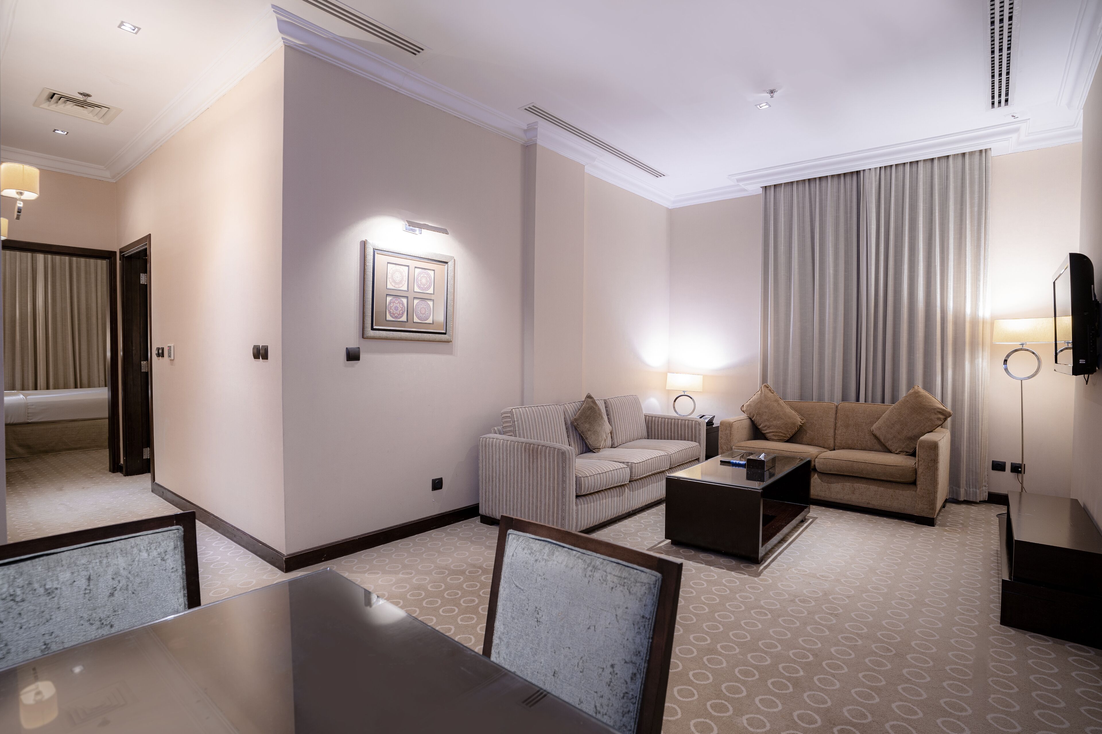 Una habitación de hotel con una mesa de comedor, dos sofás, un televisor y un cuadro en la pared.