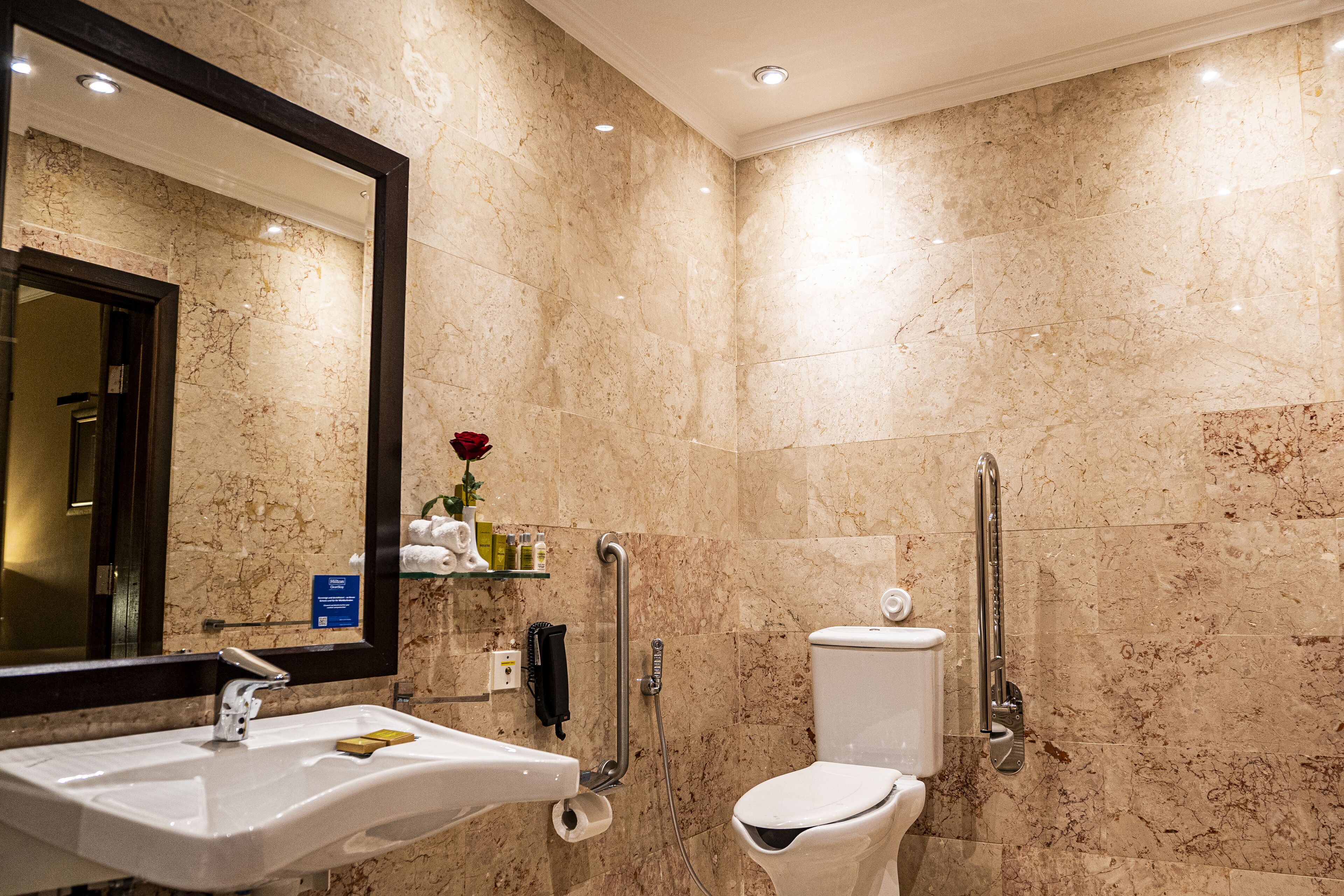 A bathroom with a marble wall, a sink, a toilet, and a shower.