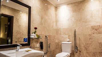 A bathroom with a marble wall, a sink, a toilet, and a shower.