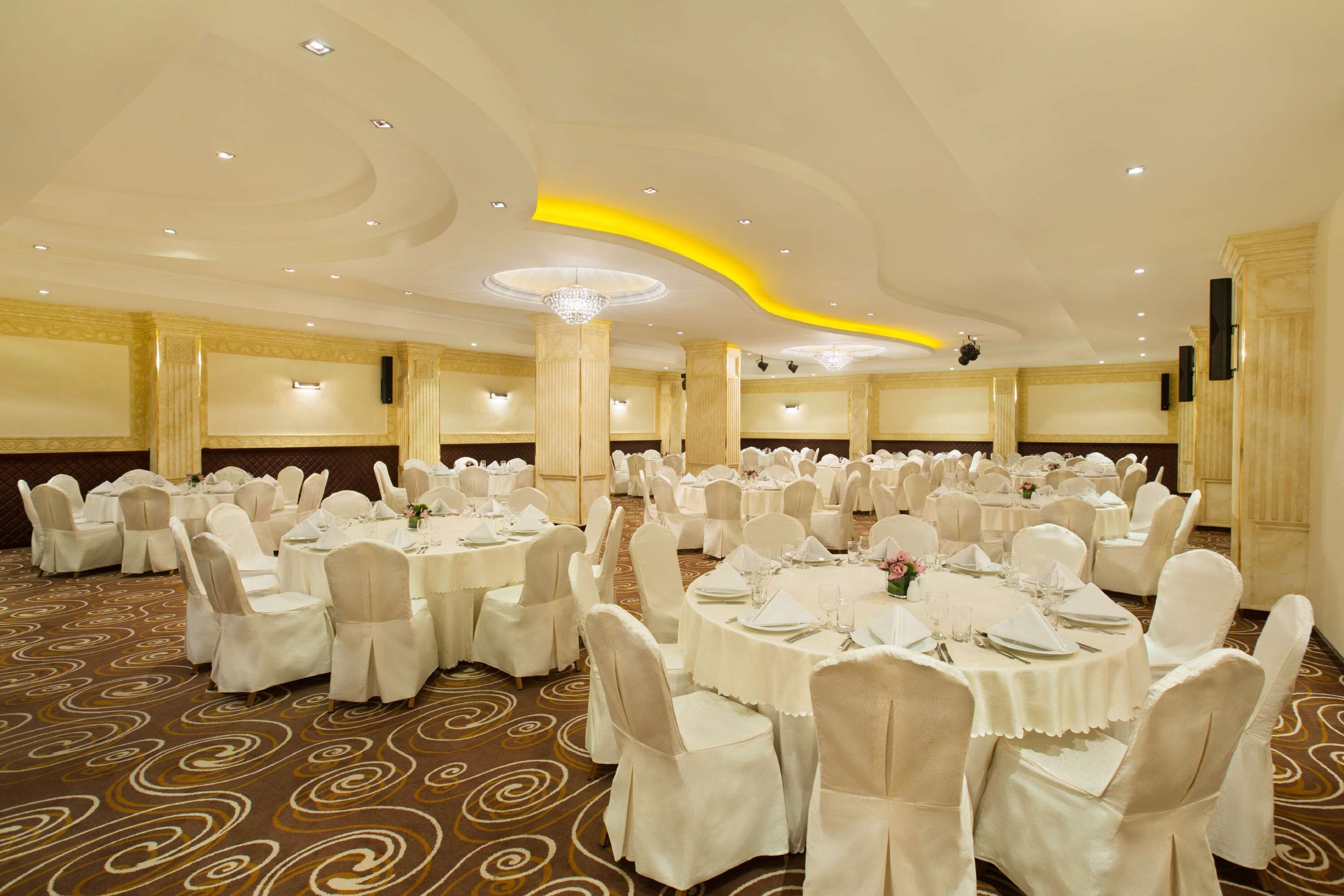 A banquet hall with round tables, white chairs, and a carpeted floor.