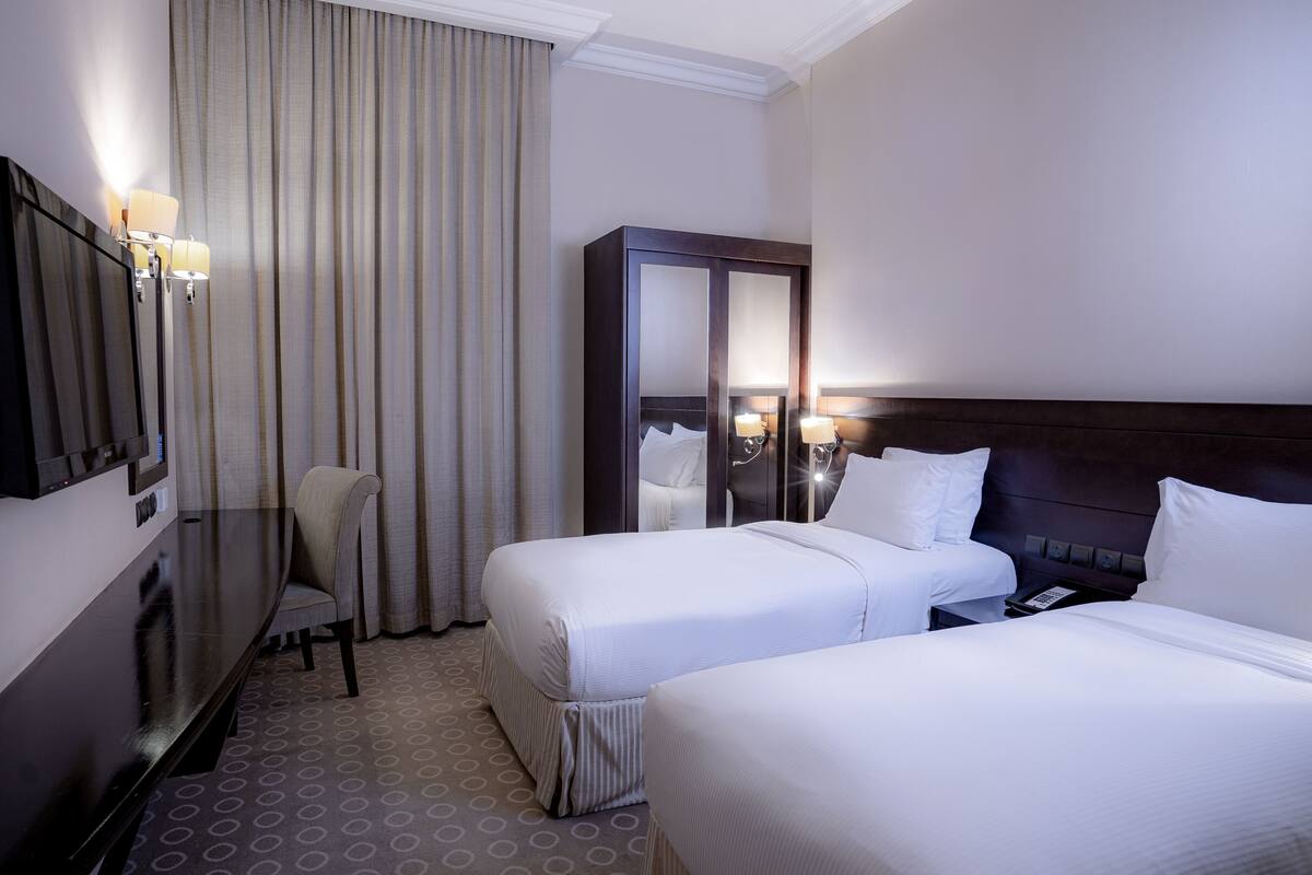 Habitación de hotel con dos camas, un escritorio, una silla y un espejo grande.