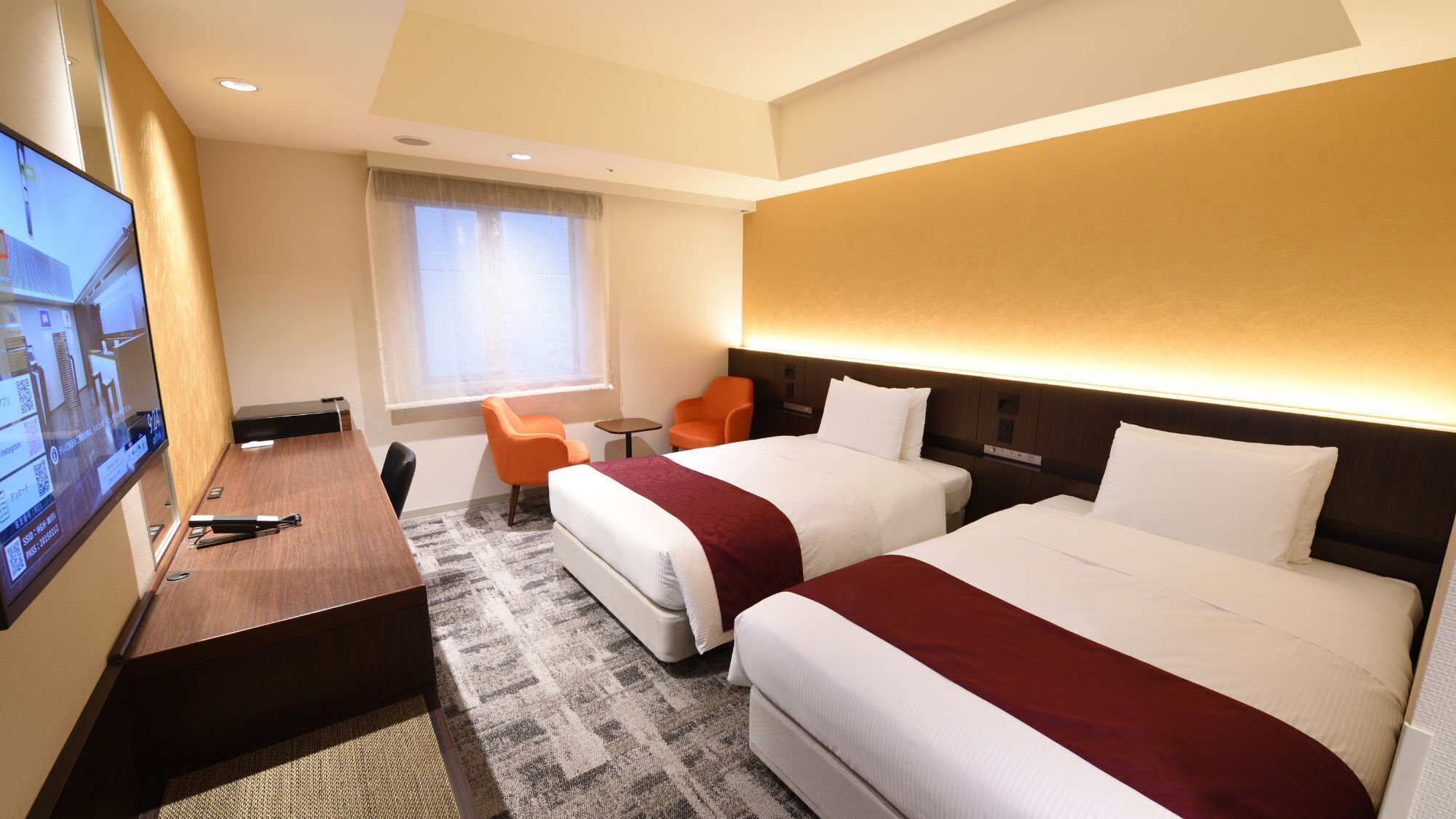 Une chambre d’hôtel avec deux lits, un bureau, une télévision et une fenêtre avec des rideaux.
