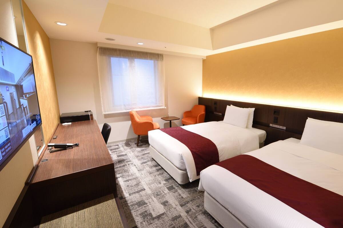 Ein Hotelzimmer mit zwei Betten, einem Schreibtisch, einem Fernseher und einem fenster mit Vorhängen.