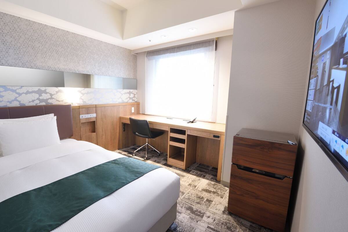 Ein Hotelzimmer mit Bett, Schreibtisch, Stuhl, Fernseher und Kleiderschrank.