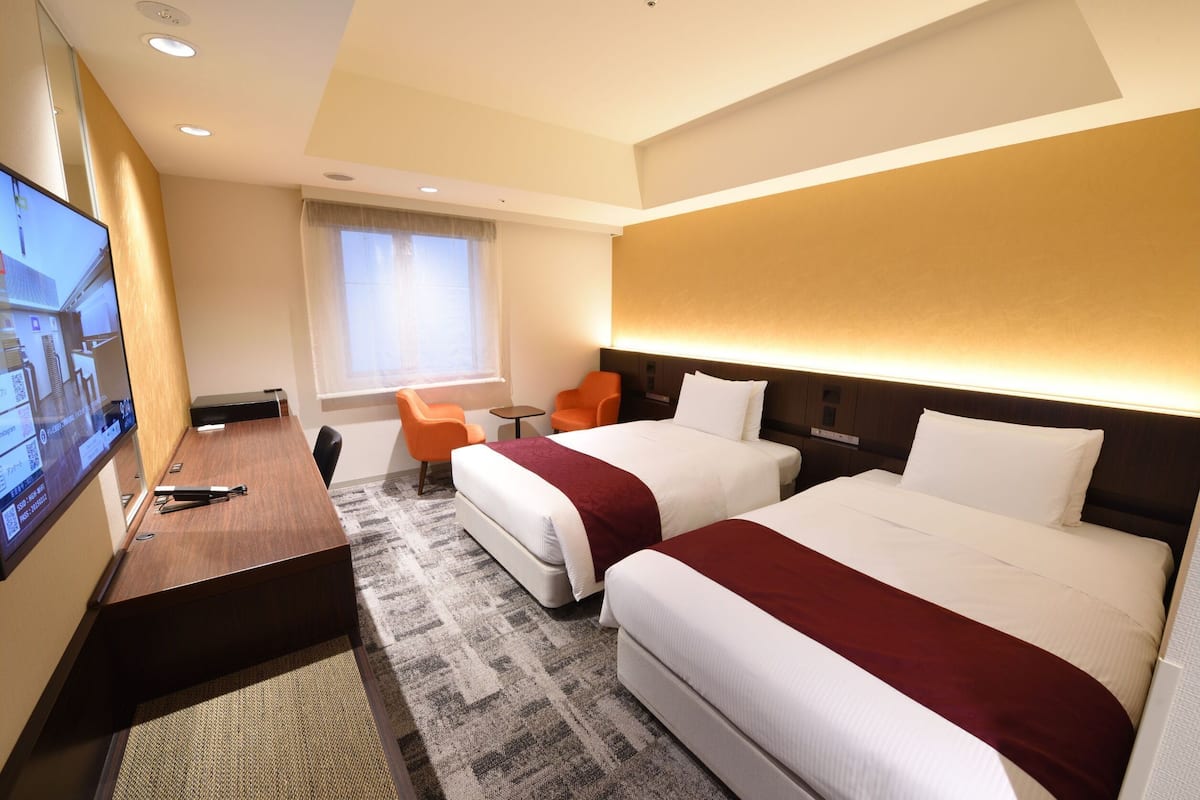 Ein Hotelzimmer mit zwei Betten, einem Schreibtisch, einem Fernseher und einem kleinen Tisch mit Stühlen.