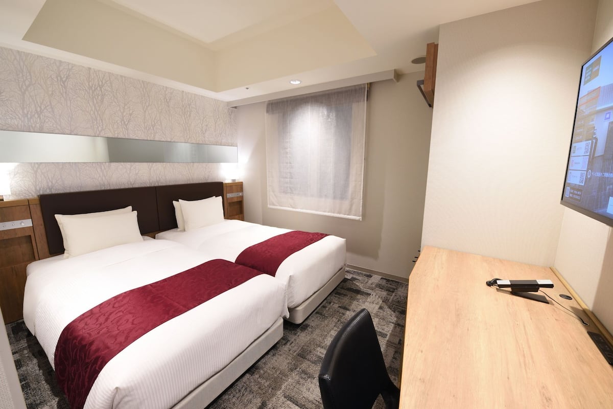 Ein Hotelzimmer mit zwei Betten, einem Schreibtisch und einem Fernseher.