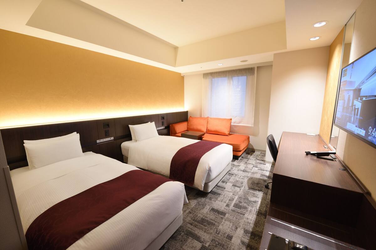 Ein Hotelzimmer mit zwei Betten, einem Schreibtisch und einem Fernseher.